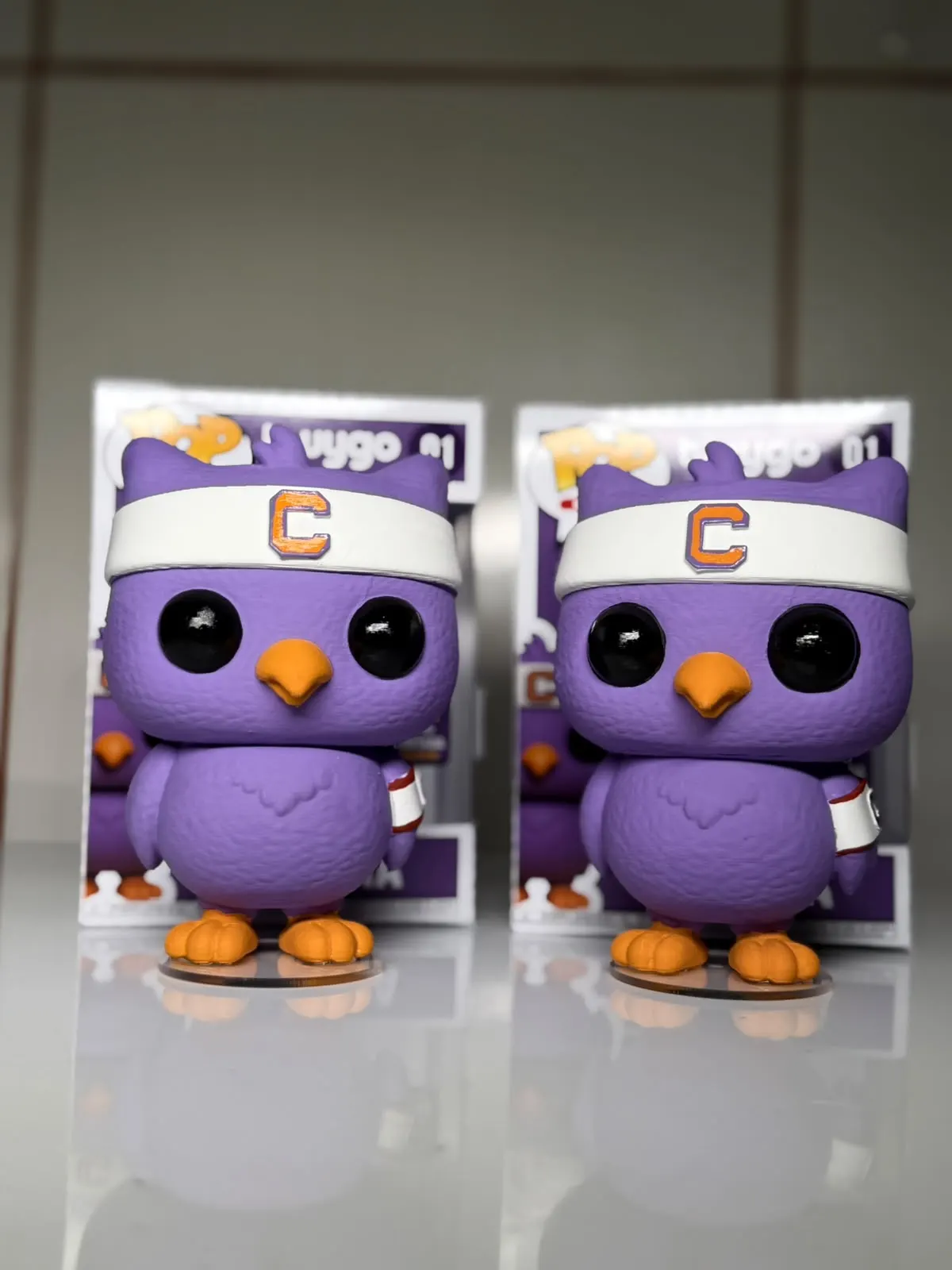 Dois mascotes roxos personalizados em impressão 3D diante das embalagens